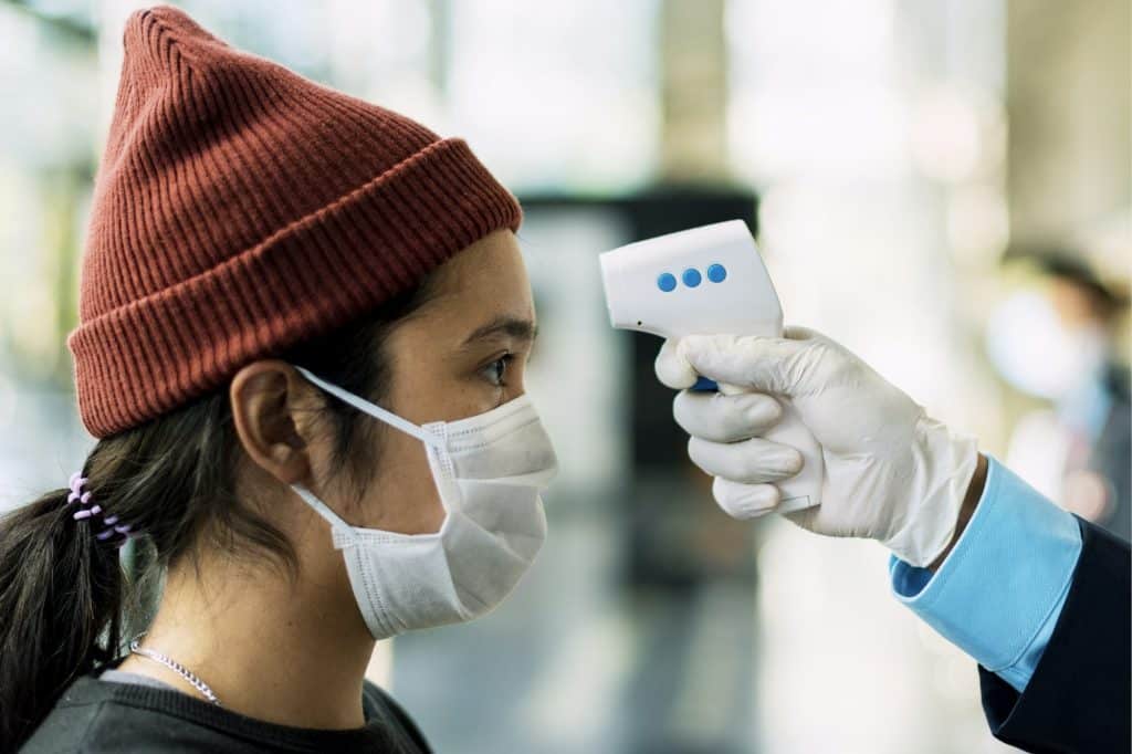 Woman in a medical mask getting her temperature measured by an electronic thermometer